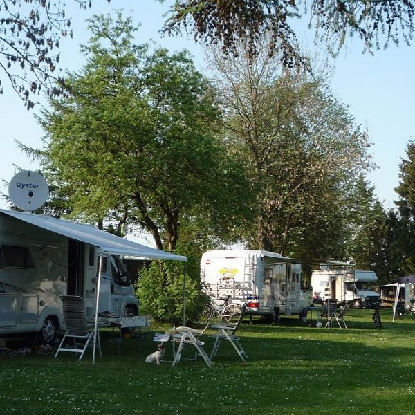 Campingwiese mit einer Reihe Wohnmobilen und deren Gartenstühlen